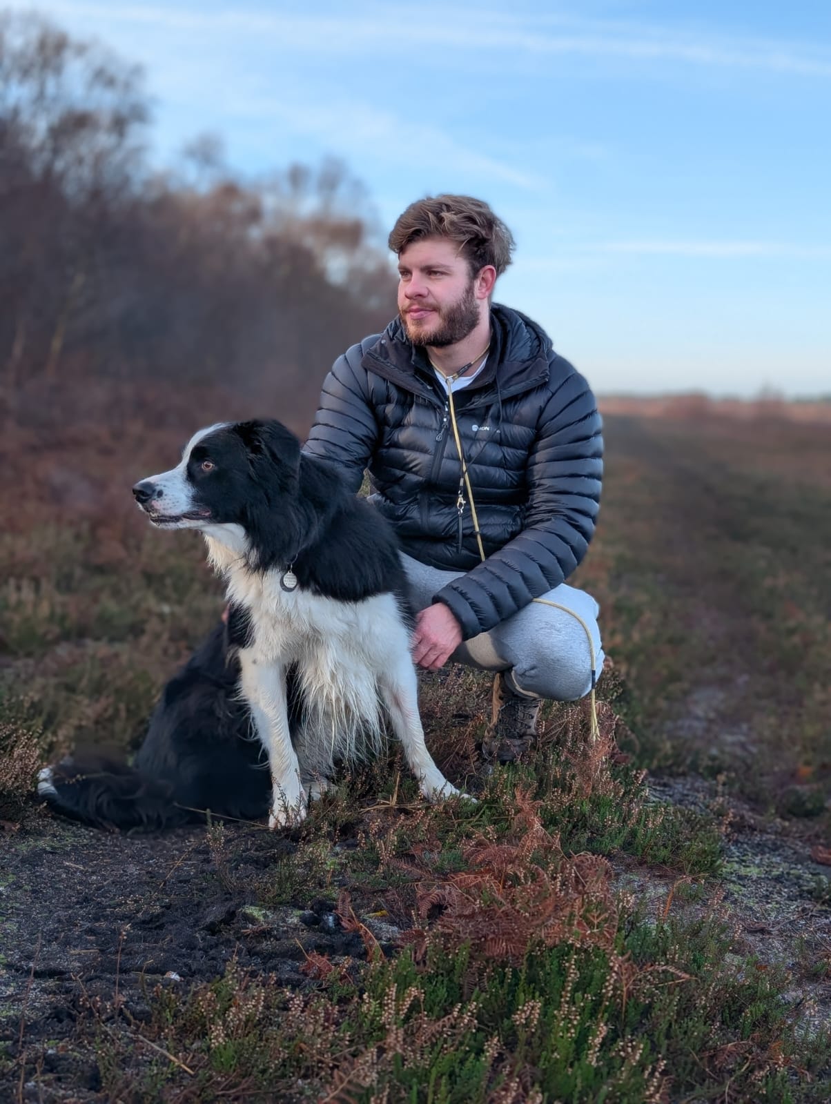 James crouching with a border collie on open moorland at golden hour